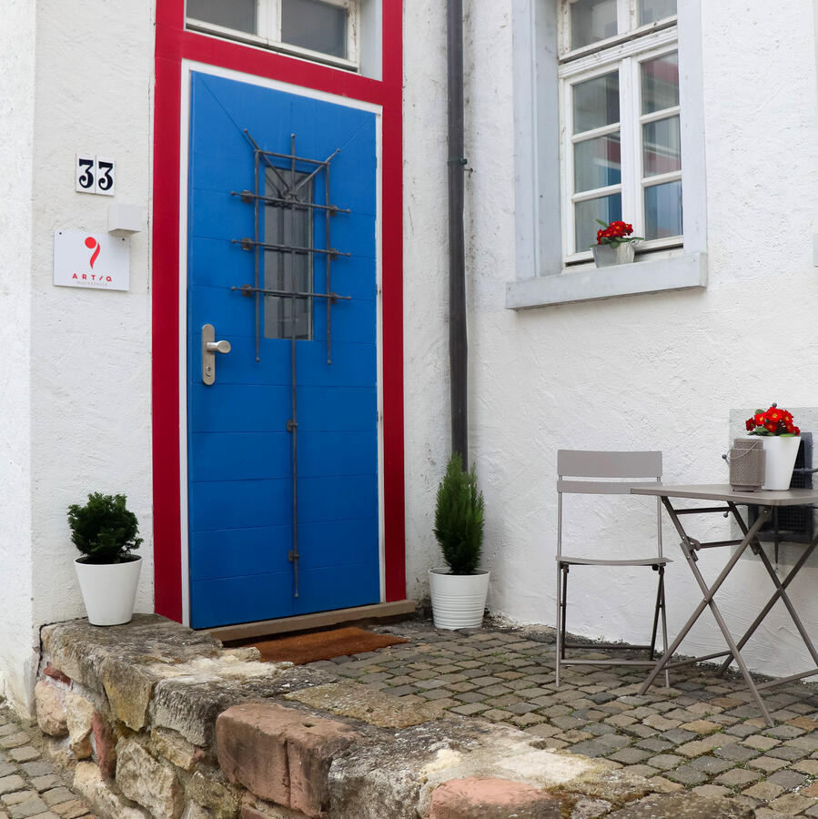 Blaue Eingangstür der ARTIQ Musikschule in der Poststraße 33 in Mainz-Finthen mit Sitzgelegenheit vor dem Gebäude.