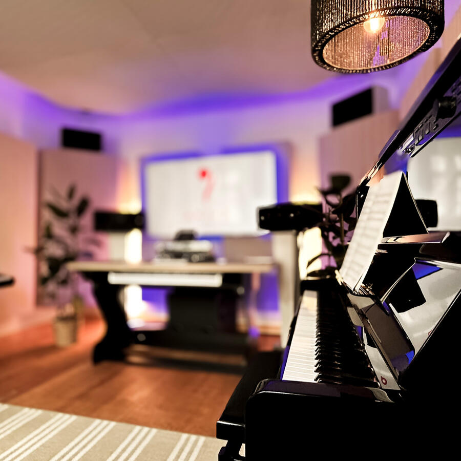 Klavierunterricht im modernen Tonstudio Mainz Perspektive vom Klavier aus auf den Unterrichtsraum mit Bildschirm, Lautsprechern und ARTIQ Logo im Hintergrund.