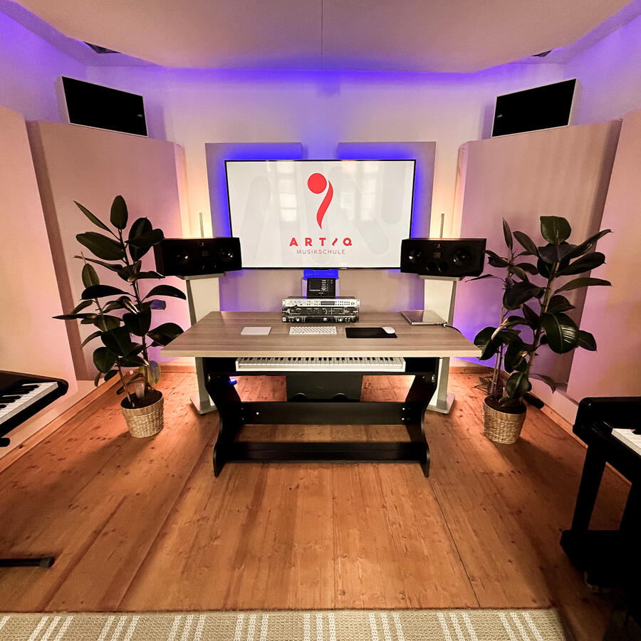 Moderner Unterrichts- und Produktionsraum der ARTIQ Musikschule mit Schreibtisch, Lautsprechern und ARTIQ Logo auf dem Bildschirm.